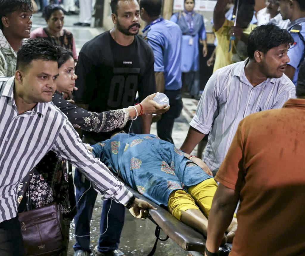 People assist an injured person on a stretcher during a stampede at Durga Puja event.