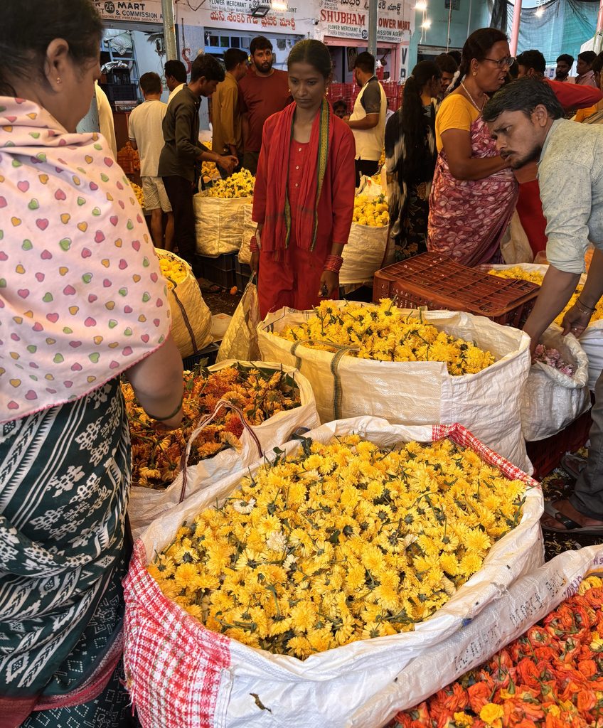 Vendors and shoppers at Gudimalkapur Flower Market with vibrant yellow flowers on display.