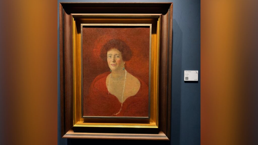 Portrait of a woman with curly hair wearing a red dress, displayed in a museum frame.