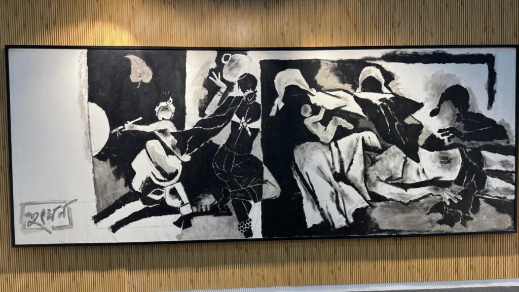 Black and white painting of musicians and dancers in traditional attire, displayed on a wall.