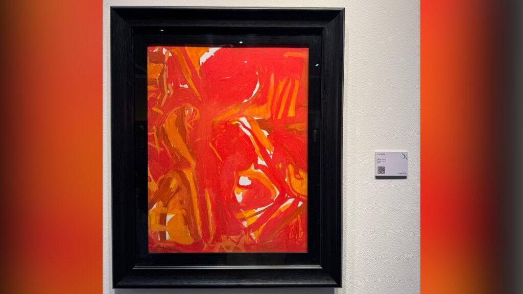 Abstract red and orange painting displayed in a black frame at an art exhibition.