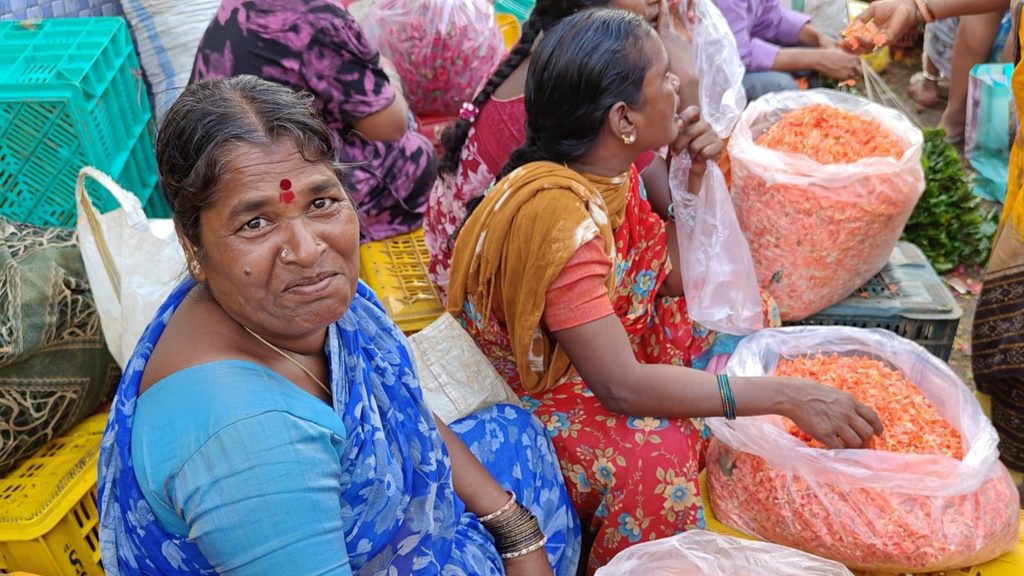 Women selling orange-colored snacks at a busy market in India.