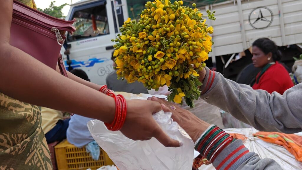 Flower vendor handing yellow flower bouquet to customer at Gudimalkapur Flower Market.