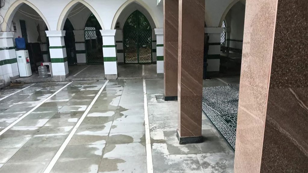 Empty mosque courtyard with white and green arches and wet tiled floor in Delhi.